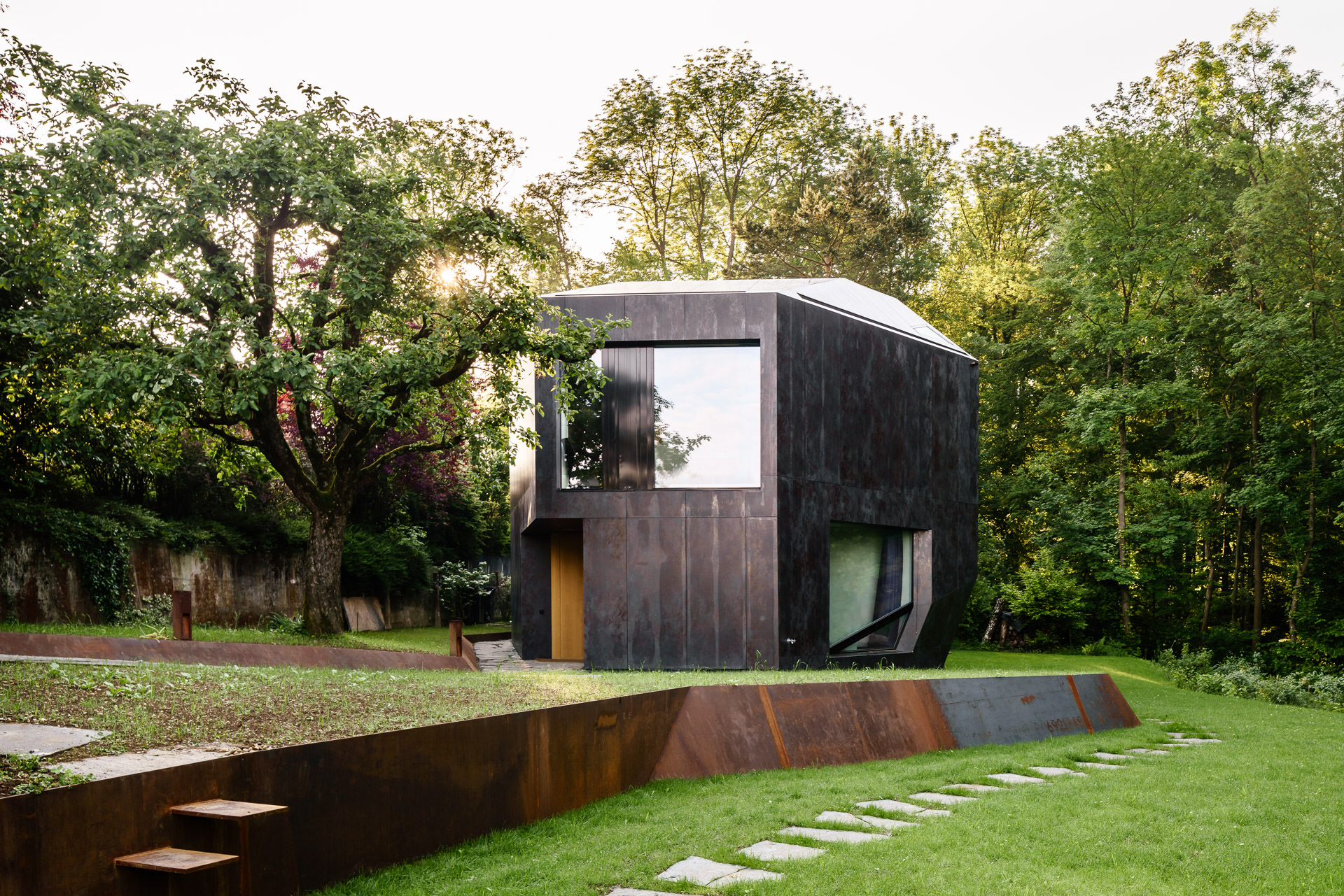 Photo of house next to the forest with metal elements separating garden segments.