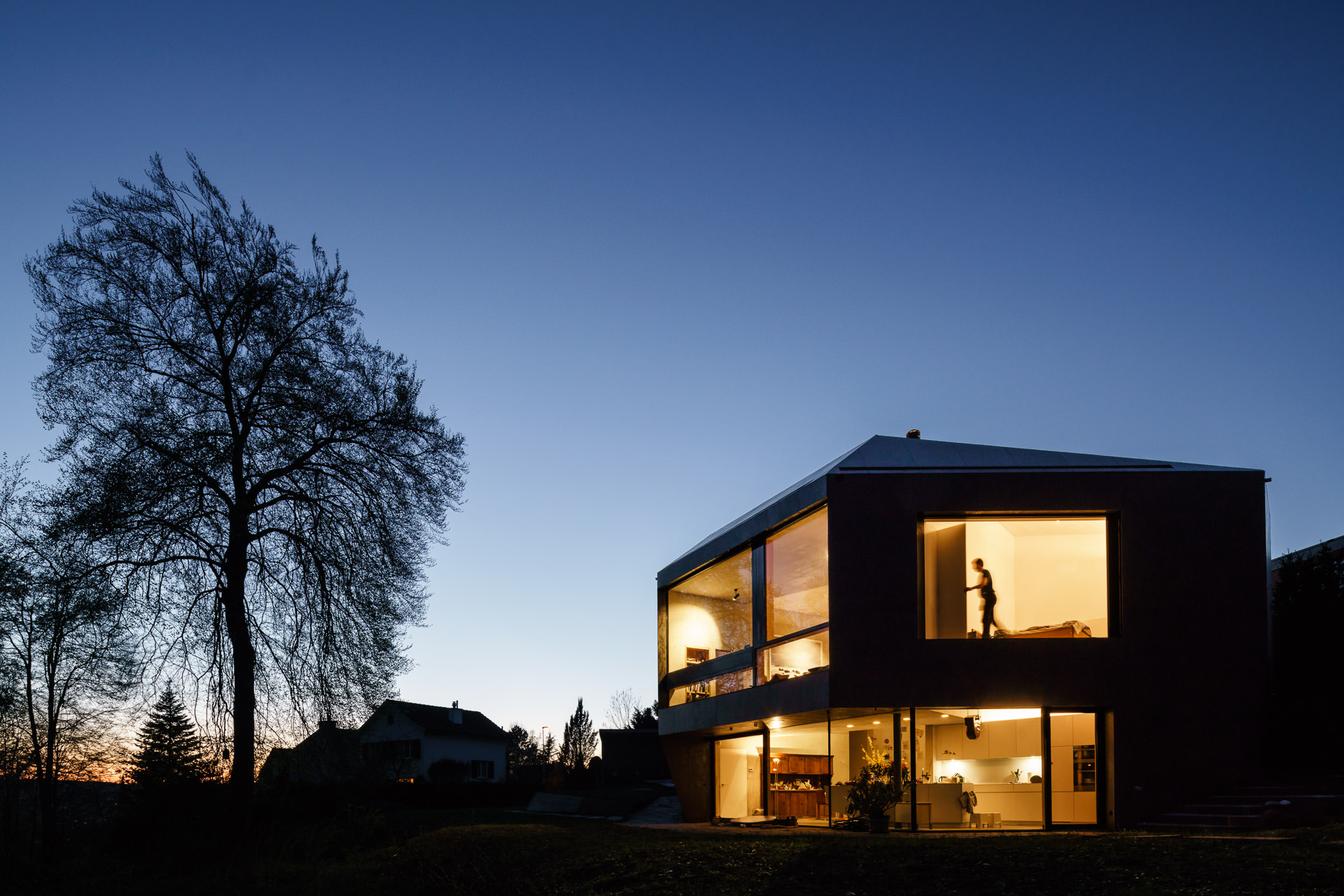 Blue hour evening view at the building with lights on and a person moving in the upper room.