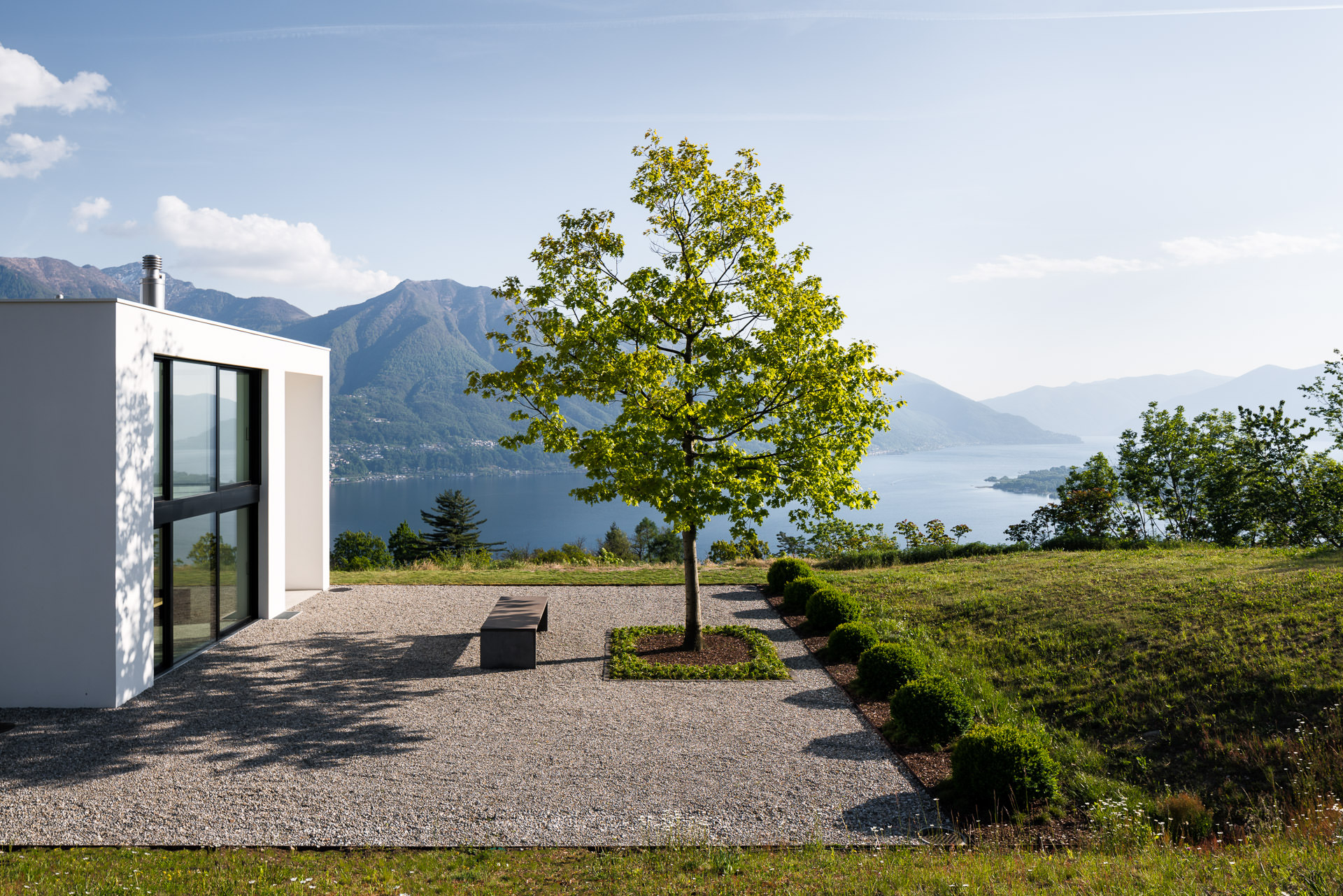 Beautiful architecture of casa nik with a beautiful, green tree and a stunning view down to lake Lago Maggiore, Ticino. Modern Architecture Photography. Design by Daluz Gonzalez & Cajos Architekten.